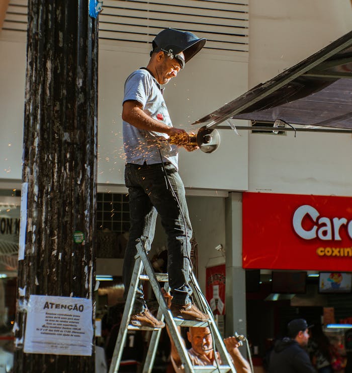 heros-img A construction worker wearing safety gear operates a grinder on a ladder outdoors.