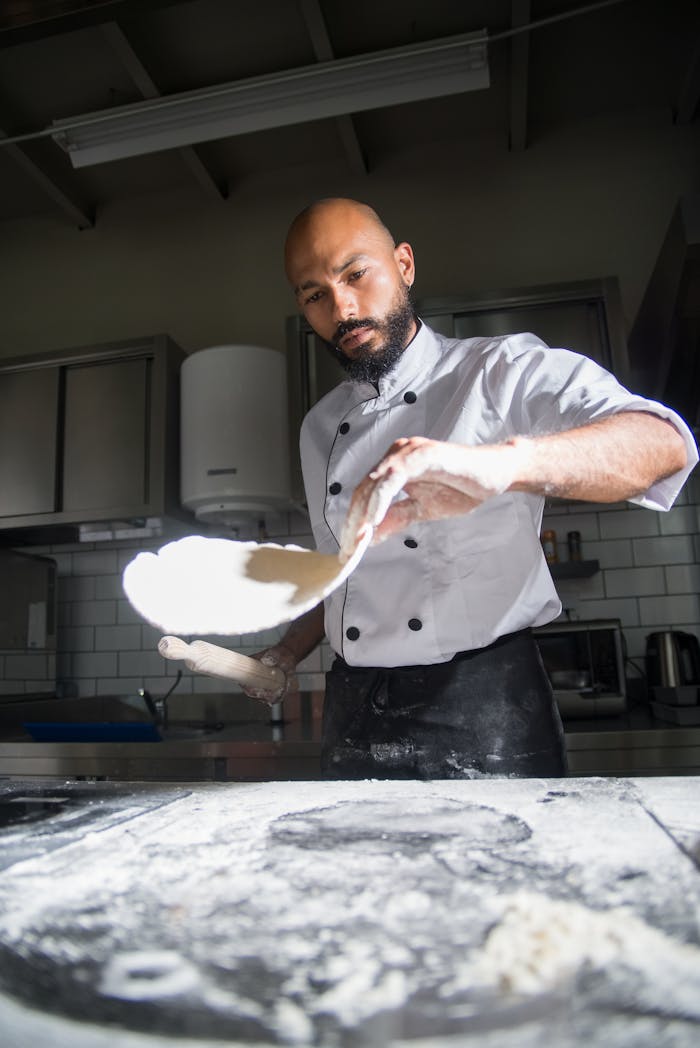about-us Chef in a modern kitchen skillfully preparing dough with precise technique. Captivating culinary artistry.